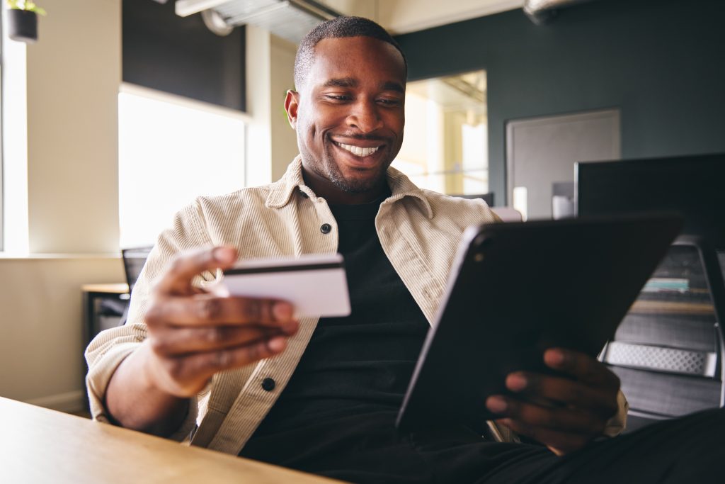 Smiling Man making online payment on tablet computer holding cre