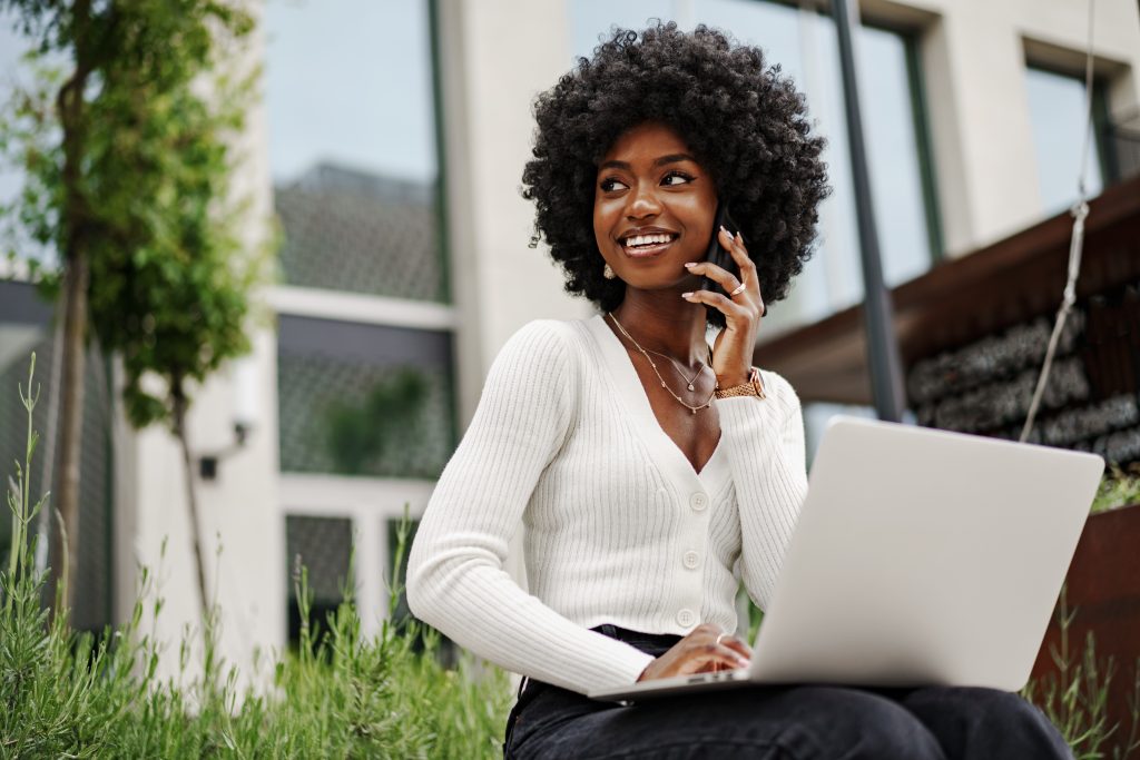 Young african american businesswoman working using laptop sitting on the bench in the city