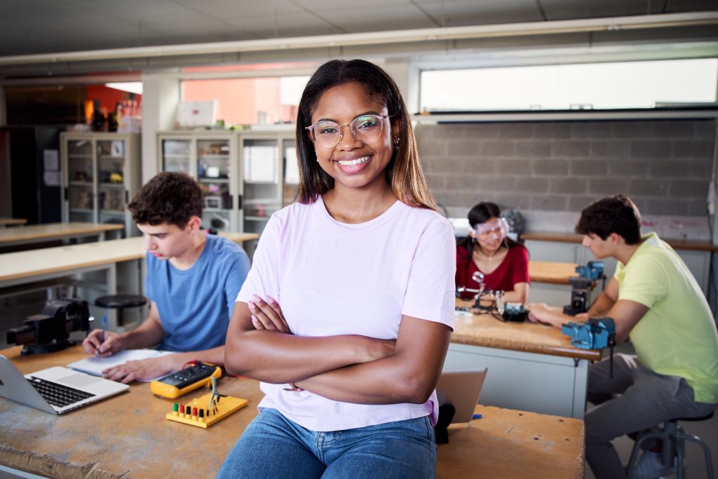 Portrait of a latina in the classroom looking at the camera with her arms crossed. Young students doing technical vocational practice in electronic class, Concept of education and technology.
