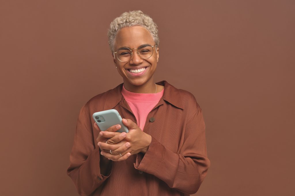 Young African American woman holding mobile phone with two hands and laughing