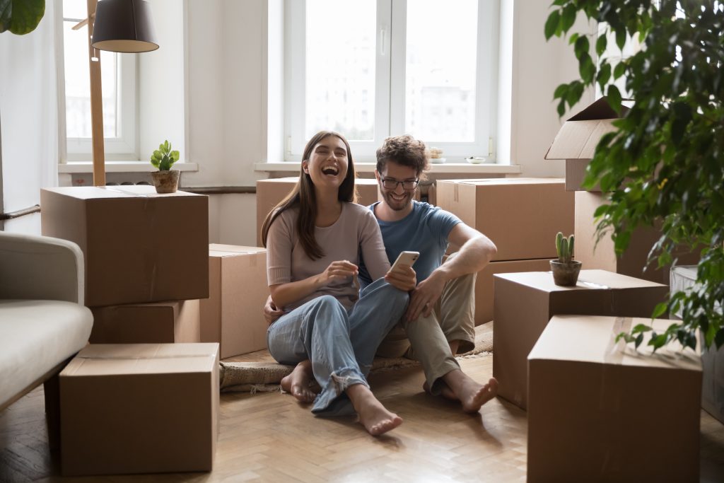 Cheerful young couple of homeowners sitting on floor at boxes