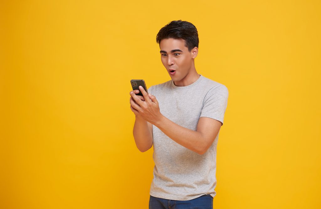 Surprised young asian man using mobile phone with positive expre
