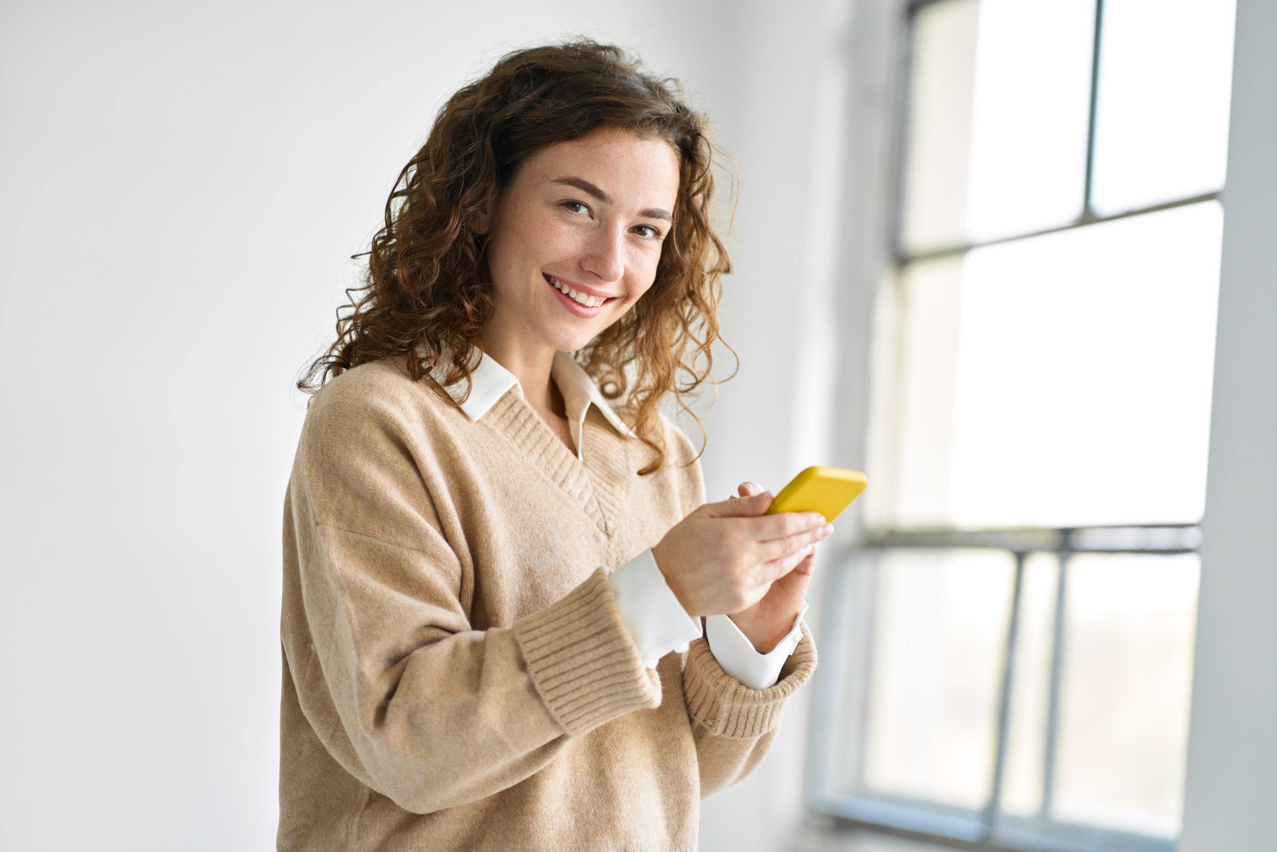 Happy young woman holding smartphone standing using mobile cell phone.