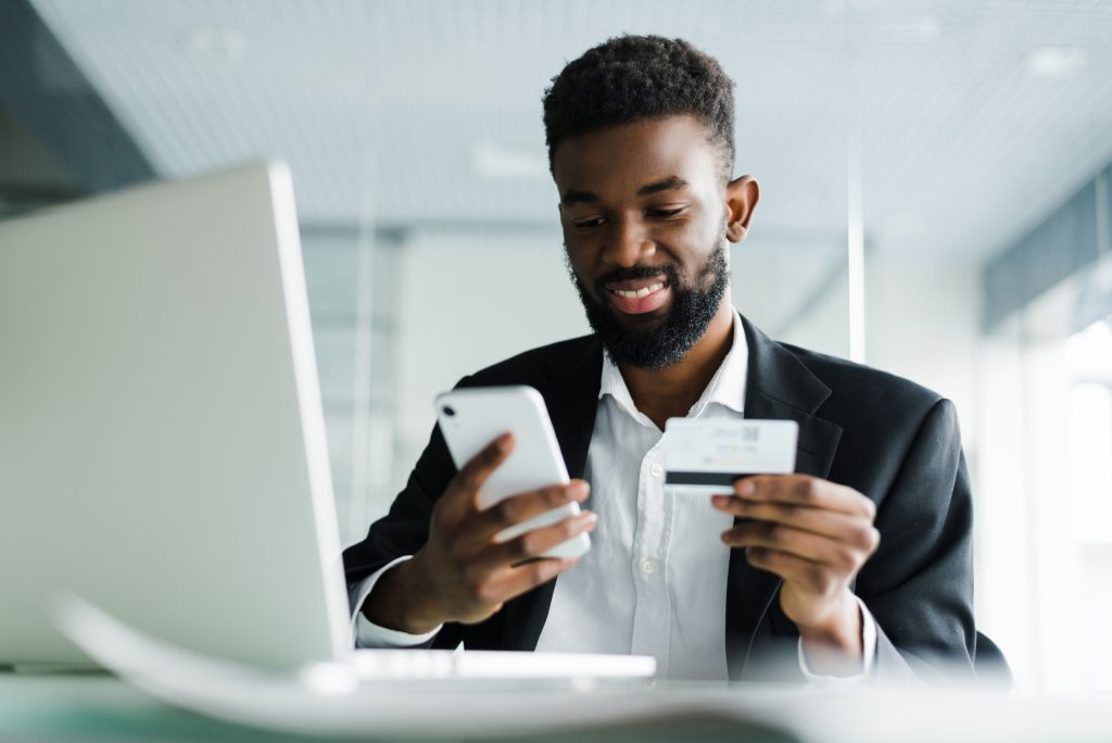 African American man paying with credit card online while making orders via mobile Internet making transaction using mobile bank application.