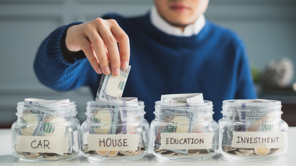 person putting money inside a glass jar labeled "house"