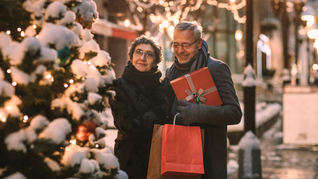 elderly couple looking at a Christmas tree while holding shopping bags
