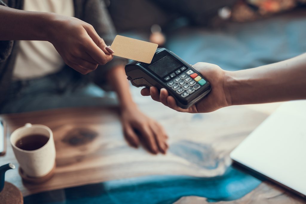 Hands of cafe visitor holding credit card and putting it to the card payment machine